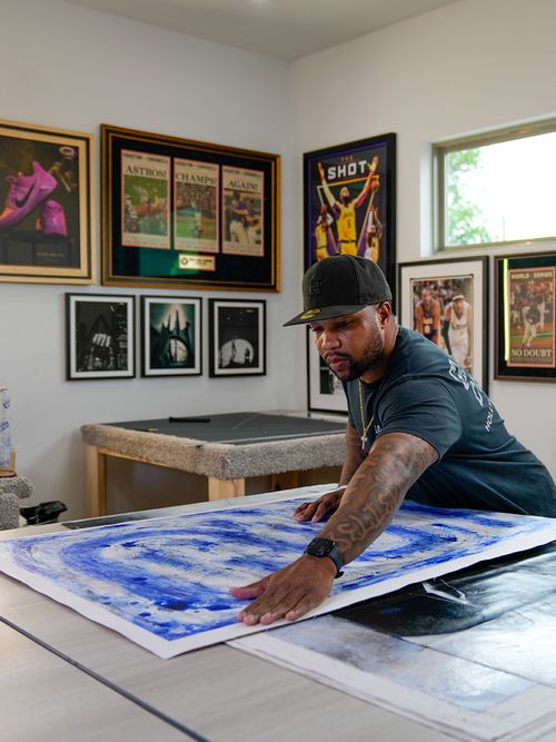 Artist smoothing blue paint on a large canvas in a bright studio with framed artwork on the walls