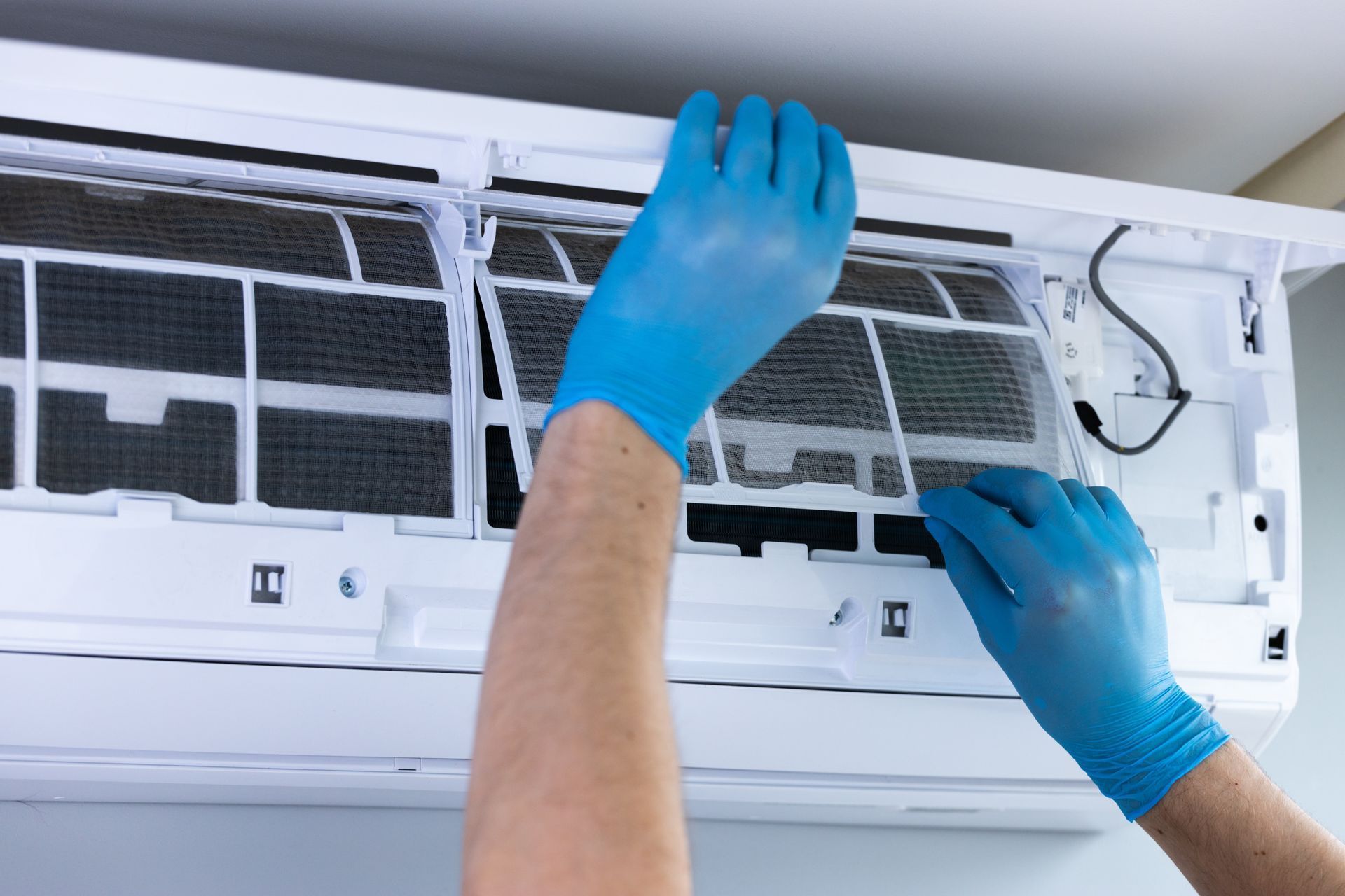 Gloved hands cleaning an air conditioner filter inside a wall-mounted unit