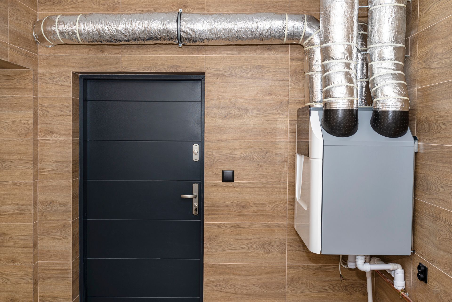 Industrial wall with a black door, silver ductwork, and gray HVAC unit.