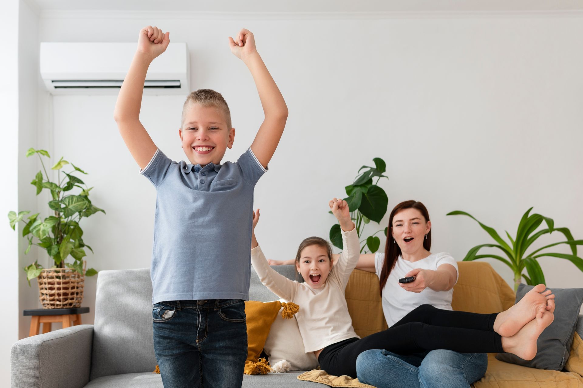 Smiling family cheering on a couch in a bright living room with houseplants and an air conditioner