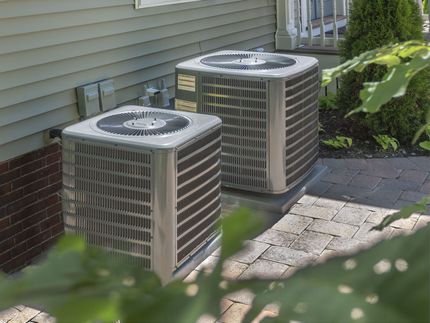 Two outdoor air conditioning units beside a house on a paved patio