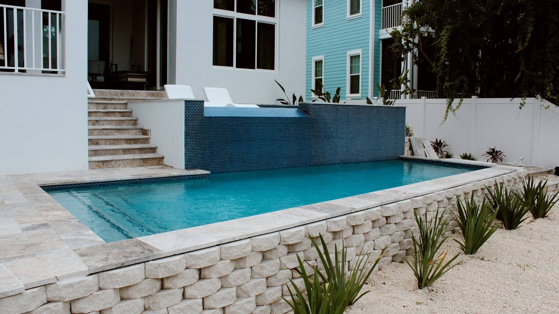 Trees and a patio surround a large swimming pool.
