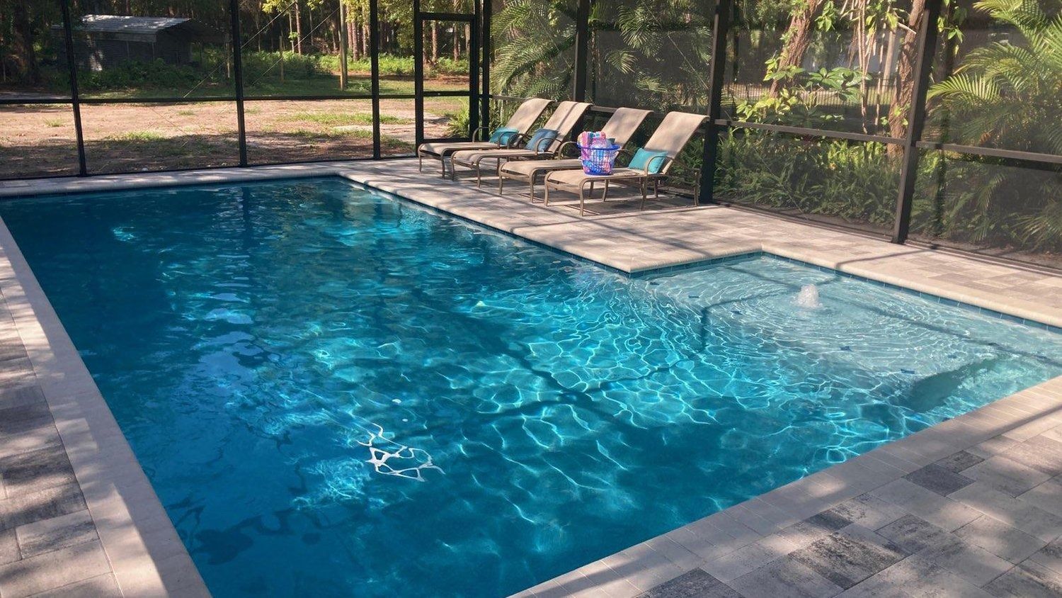 A large swimming pool with a screened in area and chairs around it.