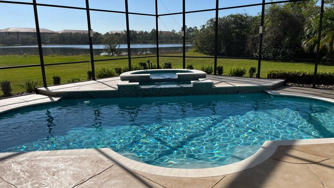 A large swimming pool surrounded by a screened in area with a view of a lake.