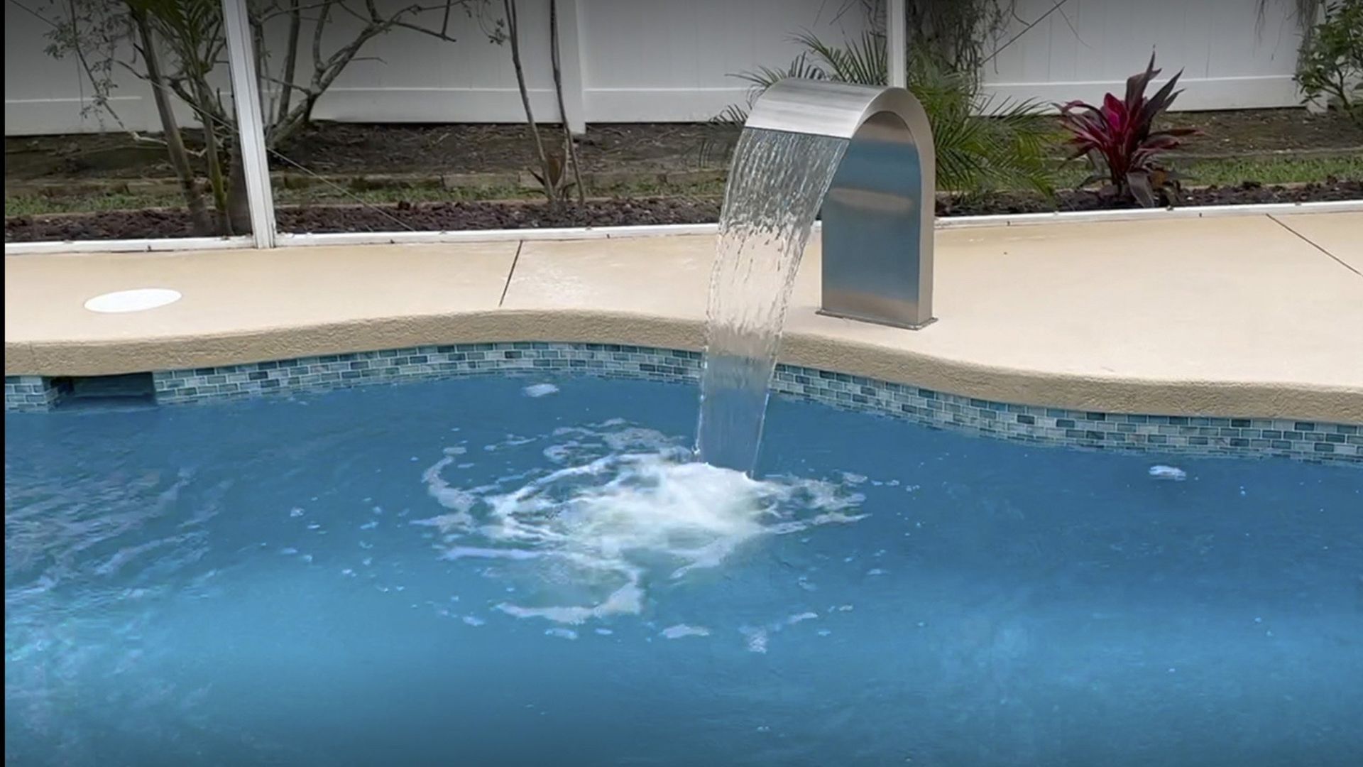 A waterfall is coming out of the side of a swimming pool.