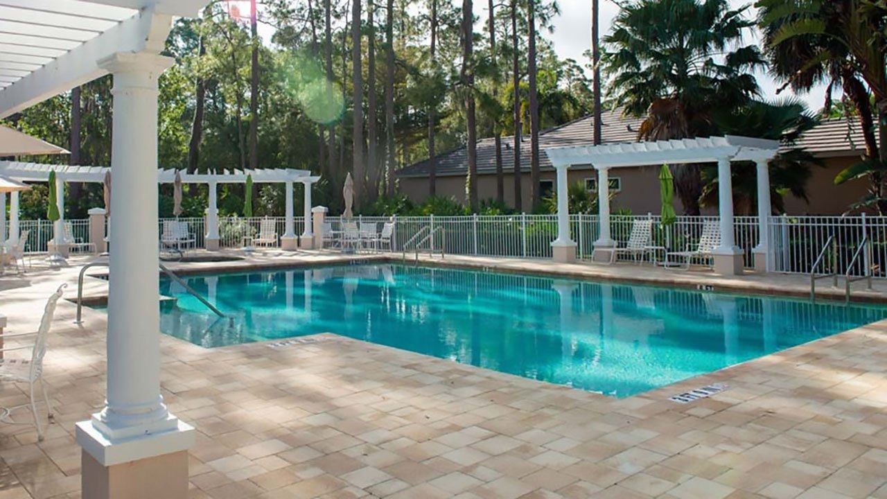A large swimming pool with a pergola and chairs around it.