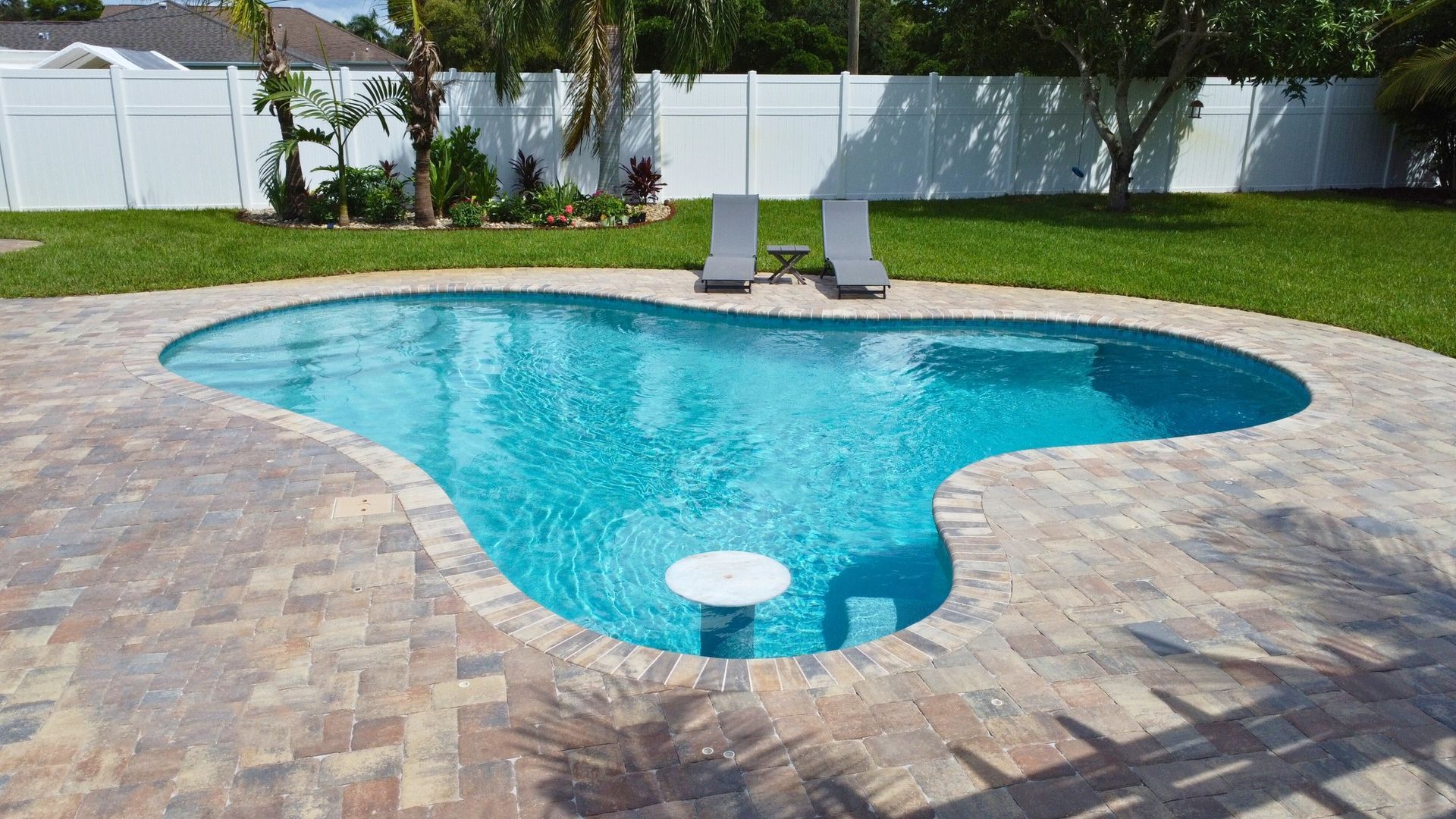 A large swimming pool is surrounded by a brick patio and chairs.