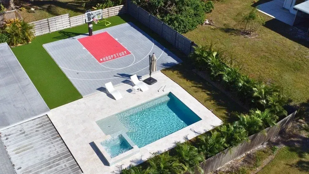 Aerial view of a backyard with a basketball court, swimming pool, and lounge chairs.
