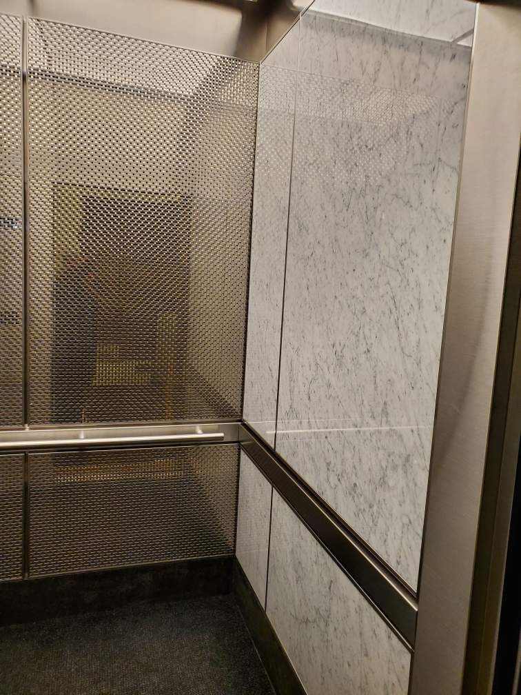 The inside of an elevator with marble walls and stainless steel rails.