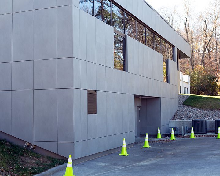 A building with a lot of windows has a lot of traffic cones in front of it