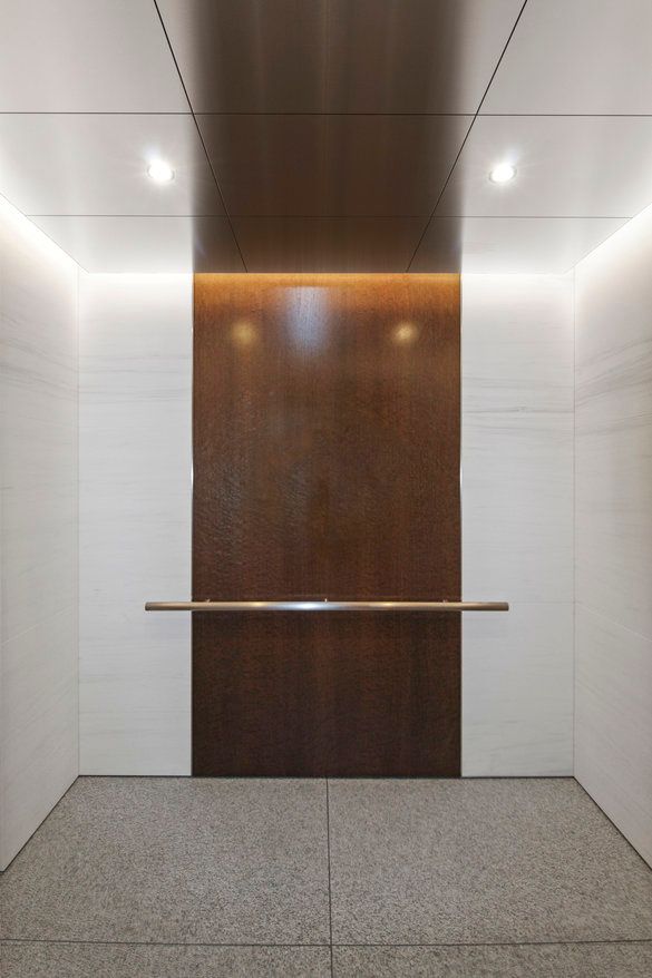 An empty elevator with a wooden wall and a stainless steel railing