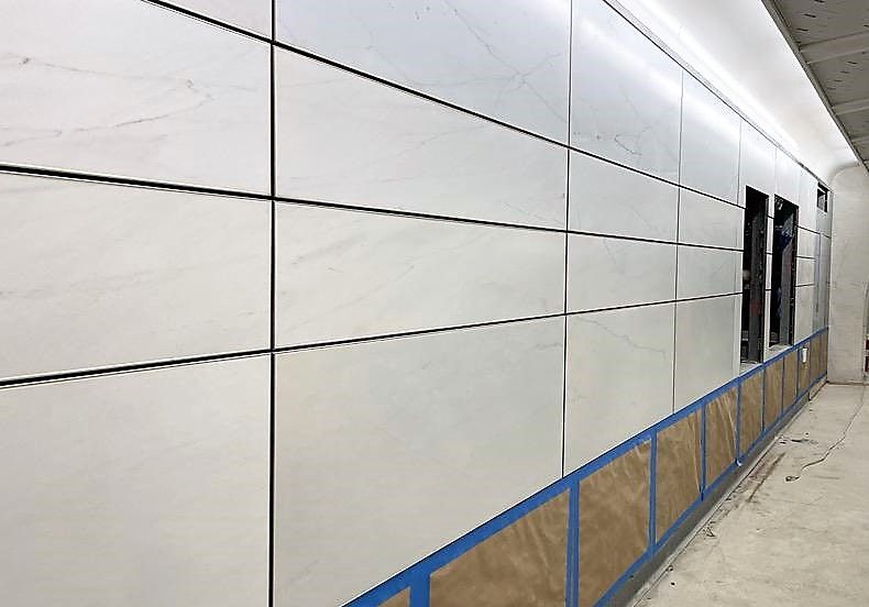 A long hallway with a white wall and blue tape on the floor.