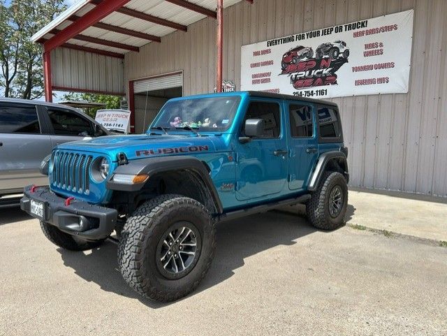 Blue lifted Jeep Wrangler parked outside a shop with a red awning and sign.