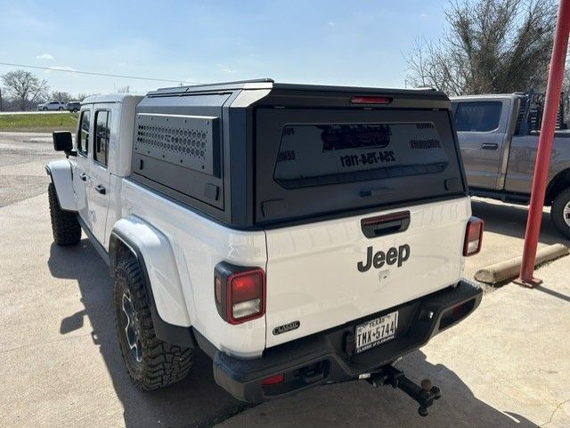 White Jeep Gladiator pickup with black topper and hitch parked outdoors on a sunny day