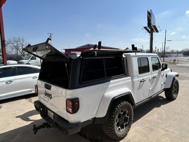 White Jeep Gladiator with black rooftop tent parked on a sunny street.
