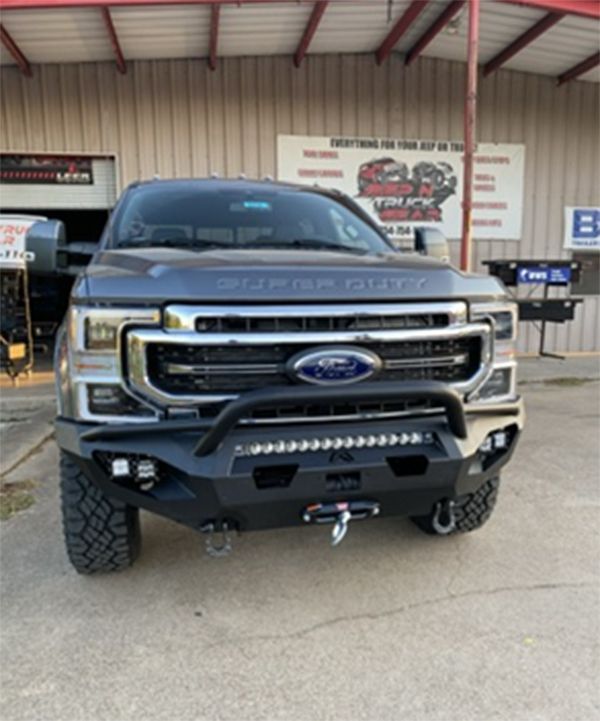 Front view of a black lifted Ford Super Duty truck parked outside a shop