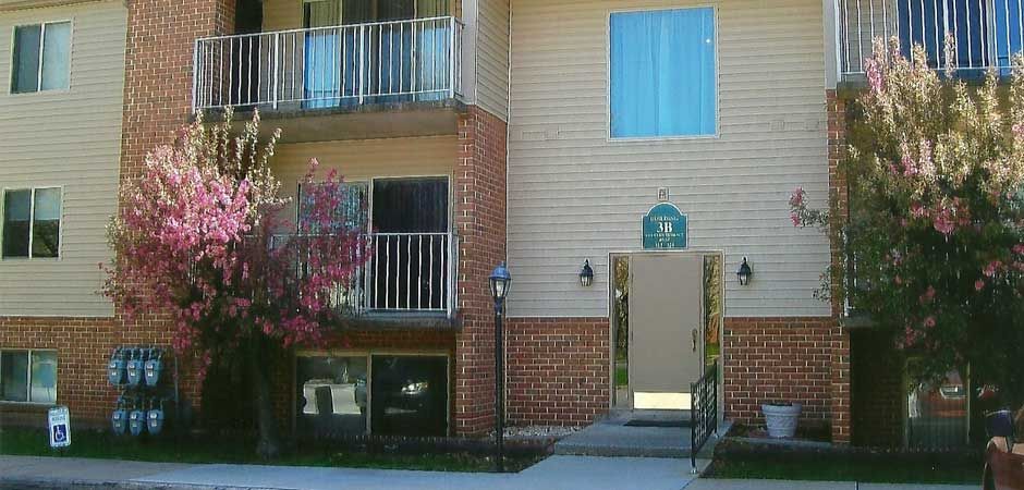 A brick apartment building with a balcony and flowers in front of it