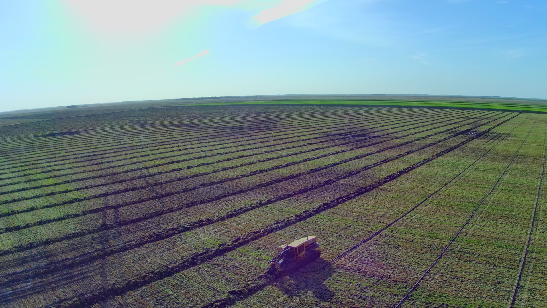 An aerial view of a tractor plowing a large green field.