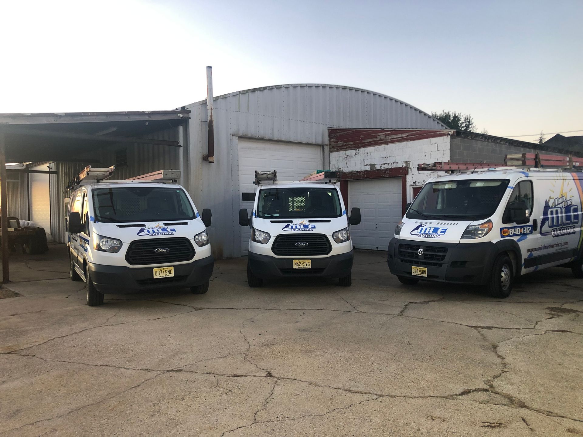 Three white service vans with company branding parked in front of a warehouse building.