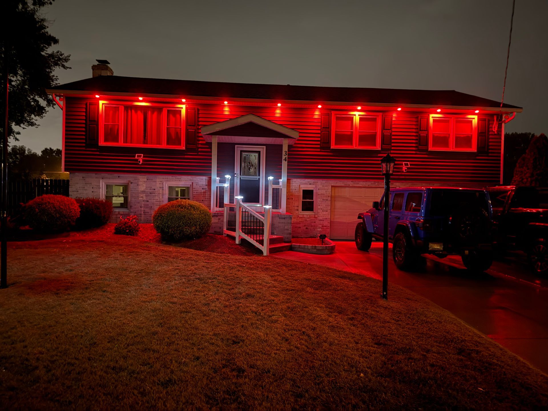 A split-level house at night illuminated by bright red accent lights under the eaves, with a Jeep parked in the driveway.