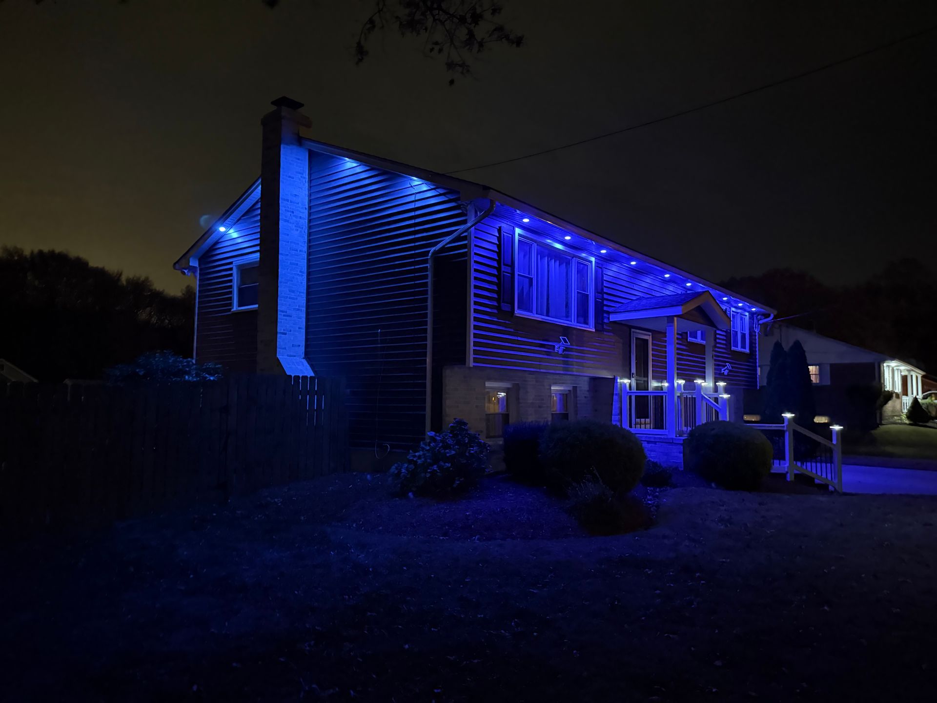 A house at night illuminated with blue outdoor lights along the roofline and porch.