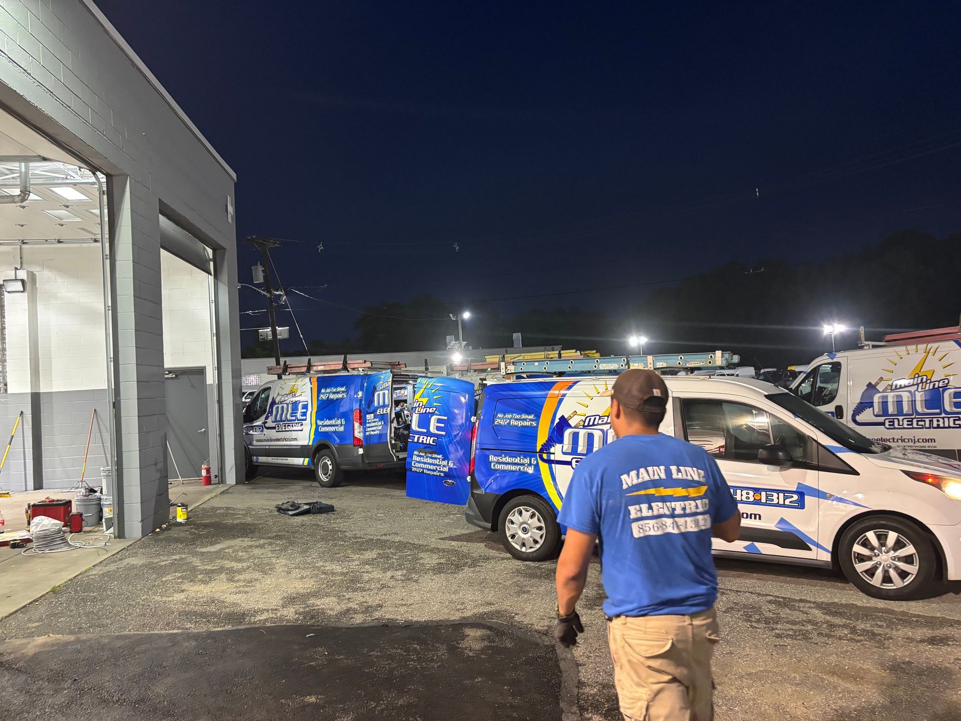 A person in a blue work shirt walking toward service vans parked outside a building at night.