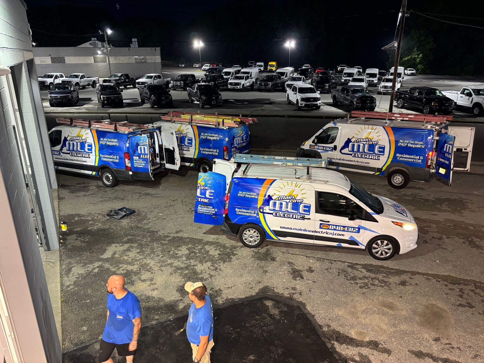 Three branded service vans parked in a dark lot at night with two people standing in the foreground.