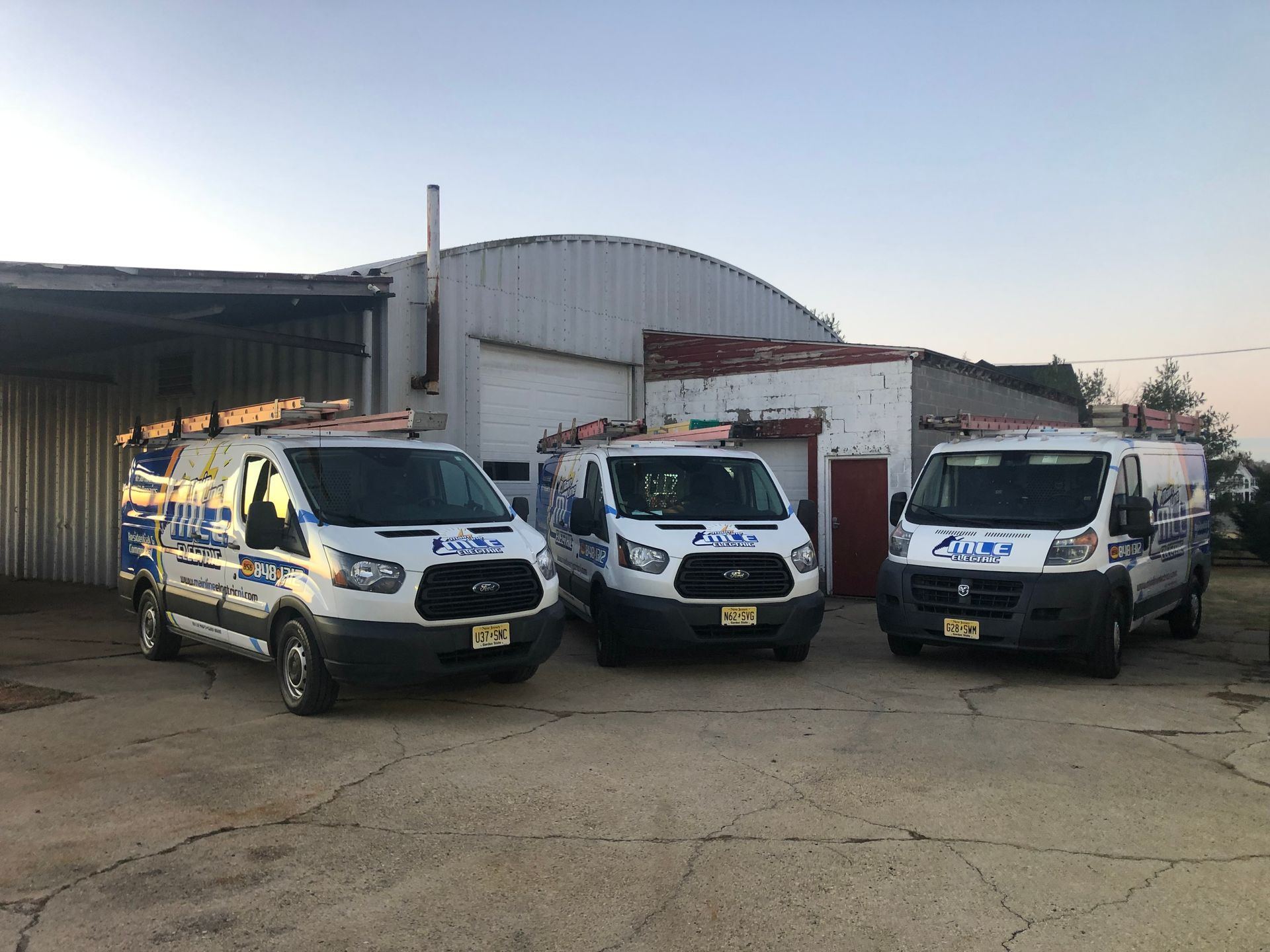 Three white company service vans parked side-by-side in front of an industrial building.