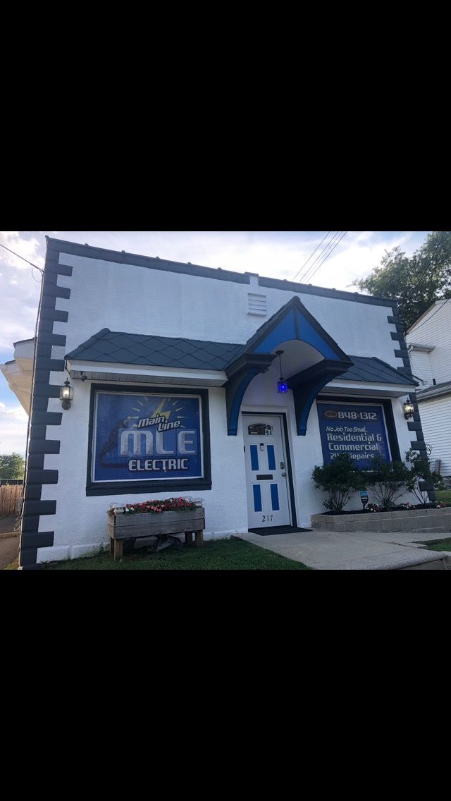A small, white storefront with dark blue trim, featuring large window signs, a central door, and a wooden bench out front.