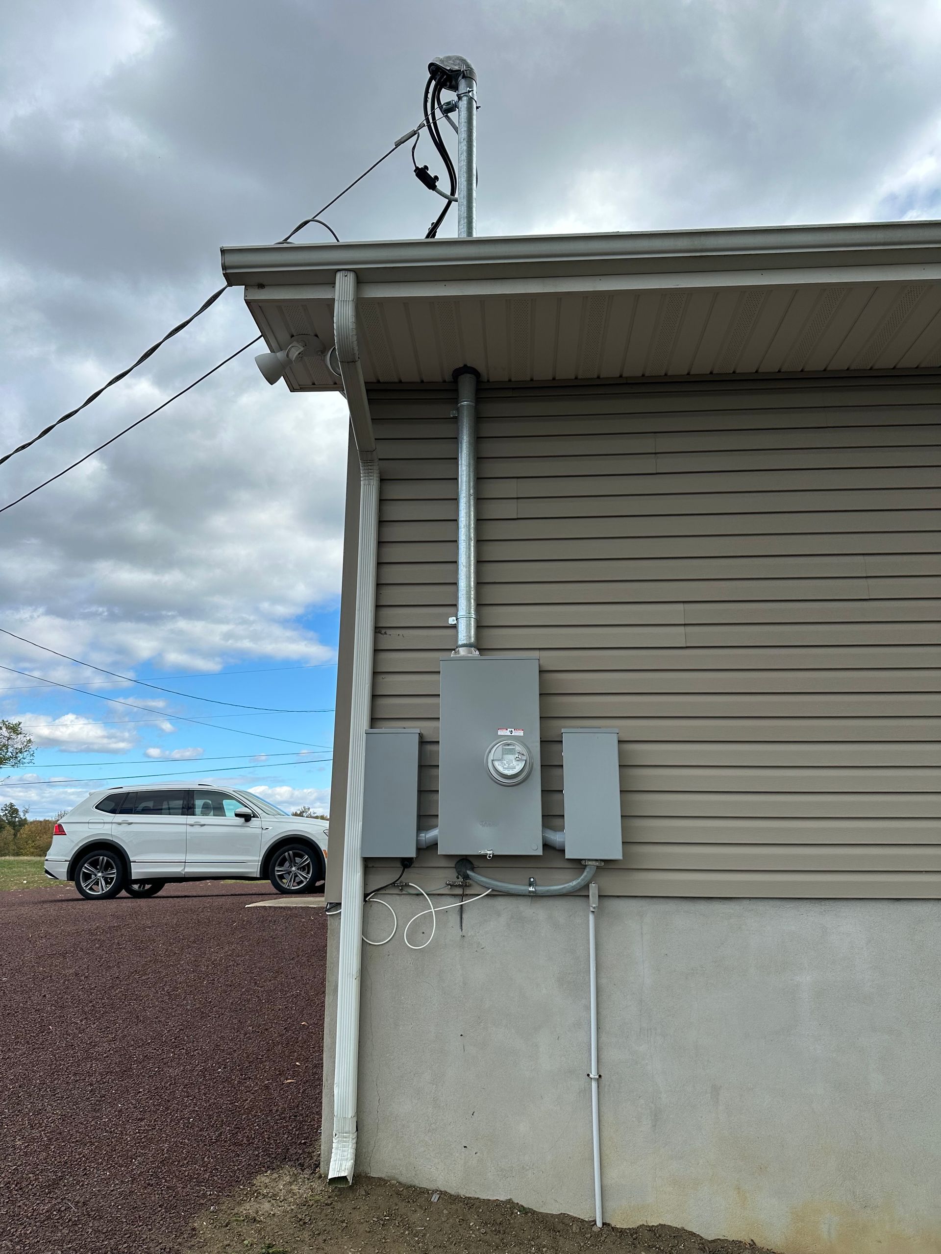 Electrical service equipment with a meter box mounted on the beige exterior wall of a building under a cloudy sky.