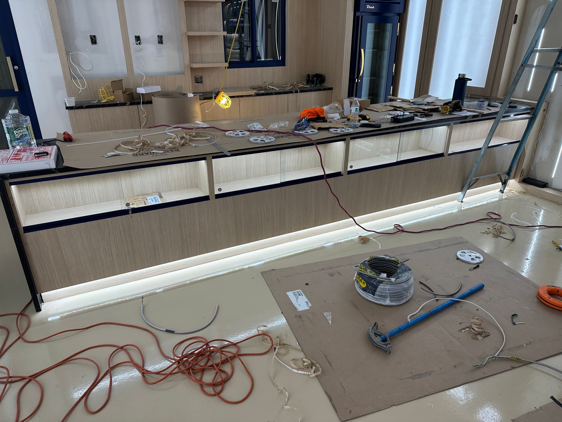 A room under construction featuring a long, wood-paneled counter with built-in LED lighting and tools on the floor.
