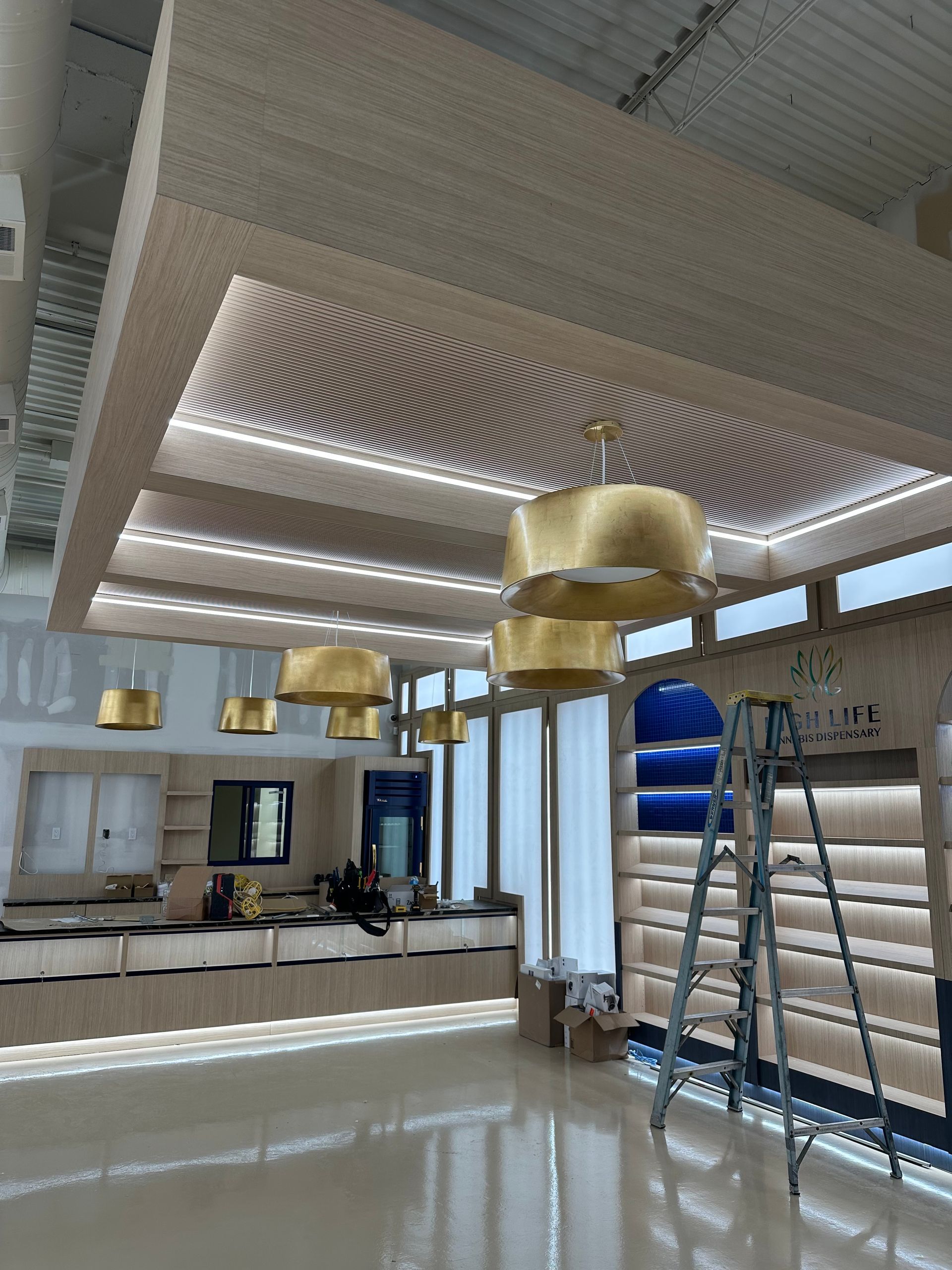 An interior retail space under construction, featuring gold pendant lights, a slatted ceiling, and a metal ladder.
