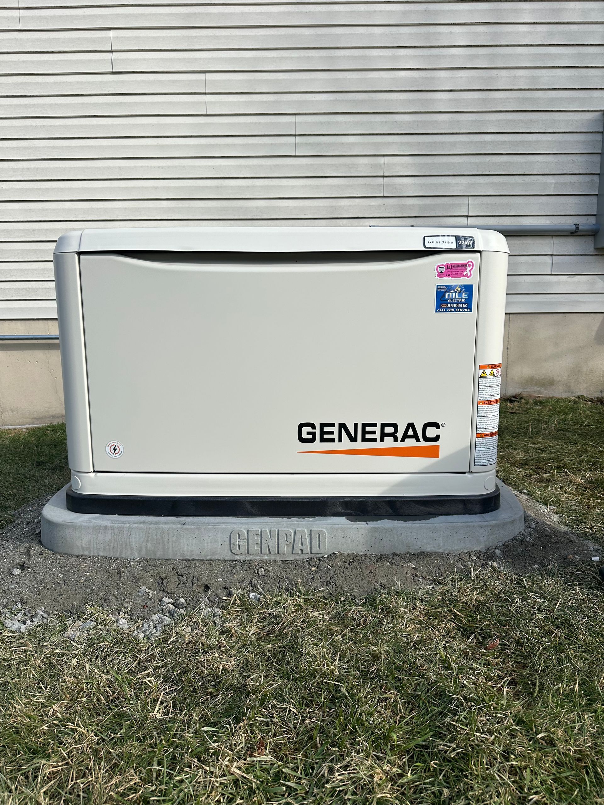 A beige Generac standby generator sits on a concrete pad in front of light-colored vinyl siding outdoors.