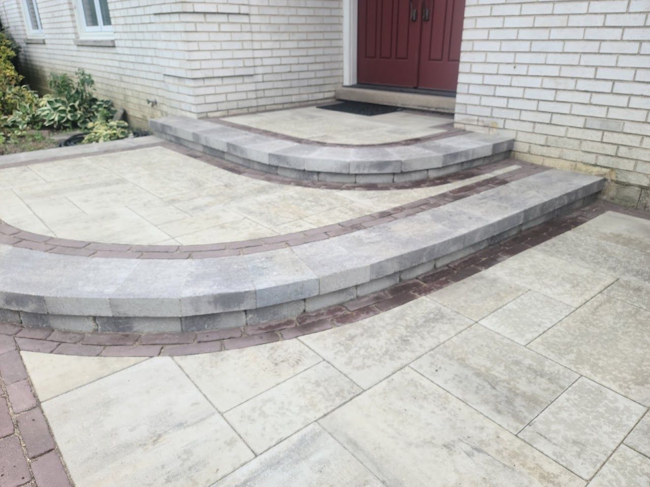 A stone patio with a curved step leading up to a house entrance with double red doors.