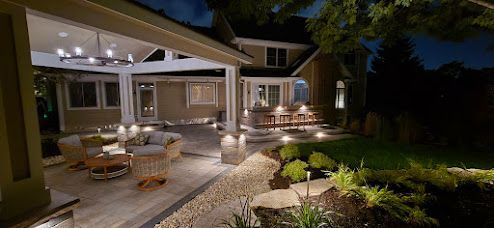 Night view of a lit patio with a covered seating area, outdoor bar, and landscaped garden.