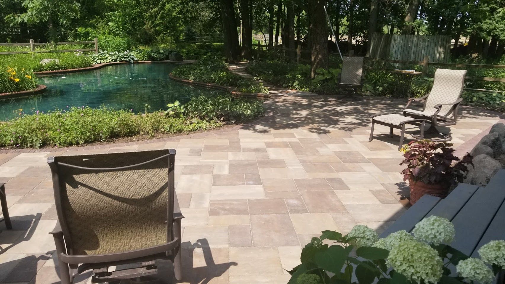 A patio with lounge chairs overlooking a pond and lush garden on a sunny day.
