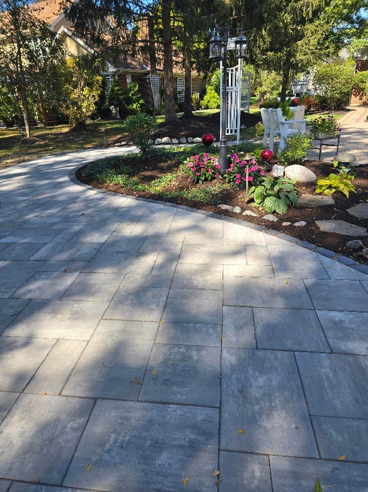 A gray stone paver walkway curves through a landscaped front yard with a garden bed, small shrubs, and a lamp post.