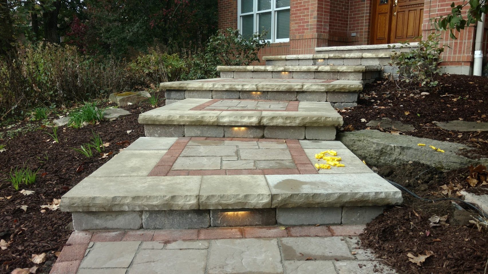 A set of stone steps leading to a house entrance, featuring integrated riser lighting and red brick decorative accents.