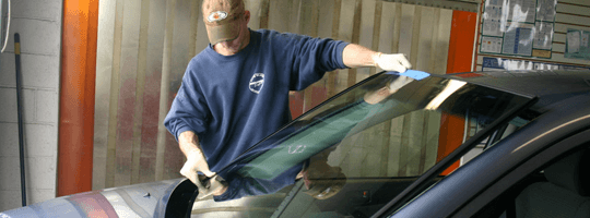 A man is cleaning the windshield of a car in a garage.