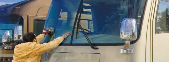 A man is cleaning the windshield of a bus.