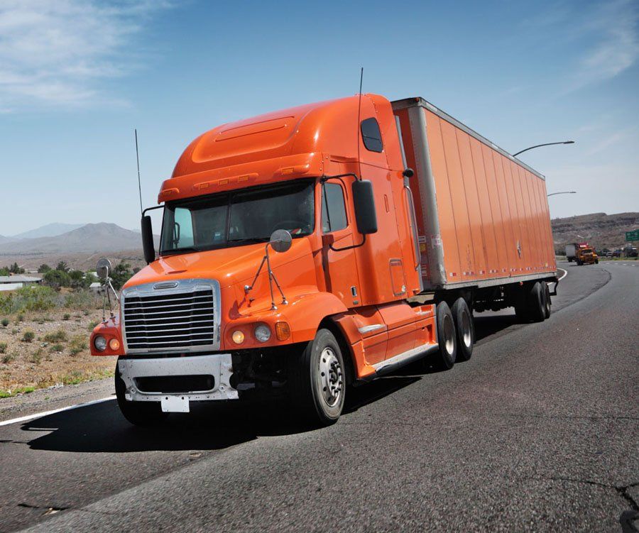 An orange semi truck is driving down a highway.