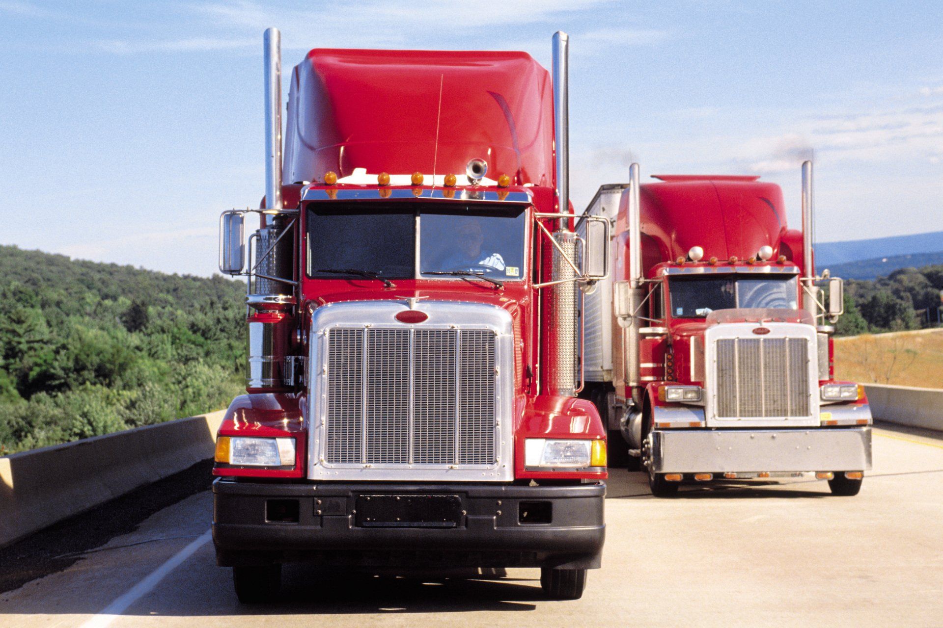 Two red semi trucks are parked on the side of the road