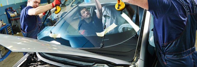 A man is installing a windshield on a car in a garage.
