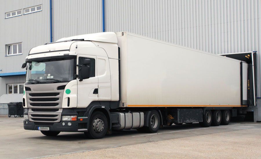 A white semi truck is parked in front of a warehouse.