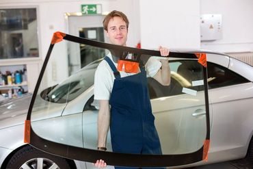 A man is holding a windshield in front of a car.