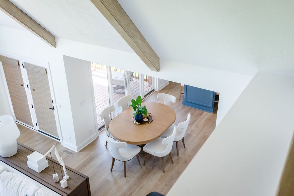 Bright dining area with round wooden table, white chairs, blue sofa, and exposed ceiling beams