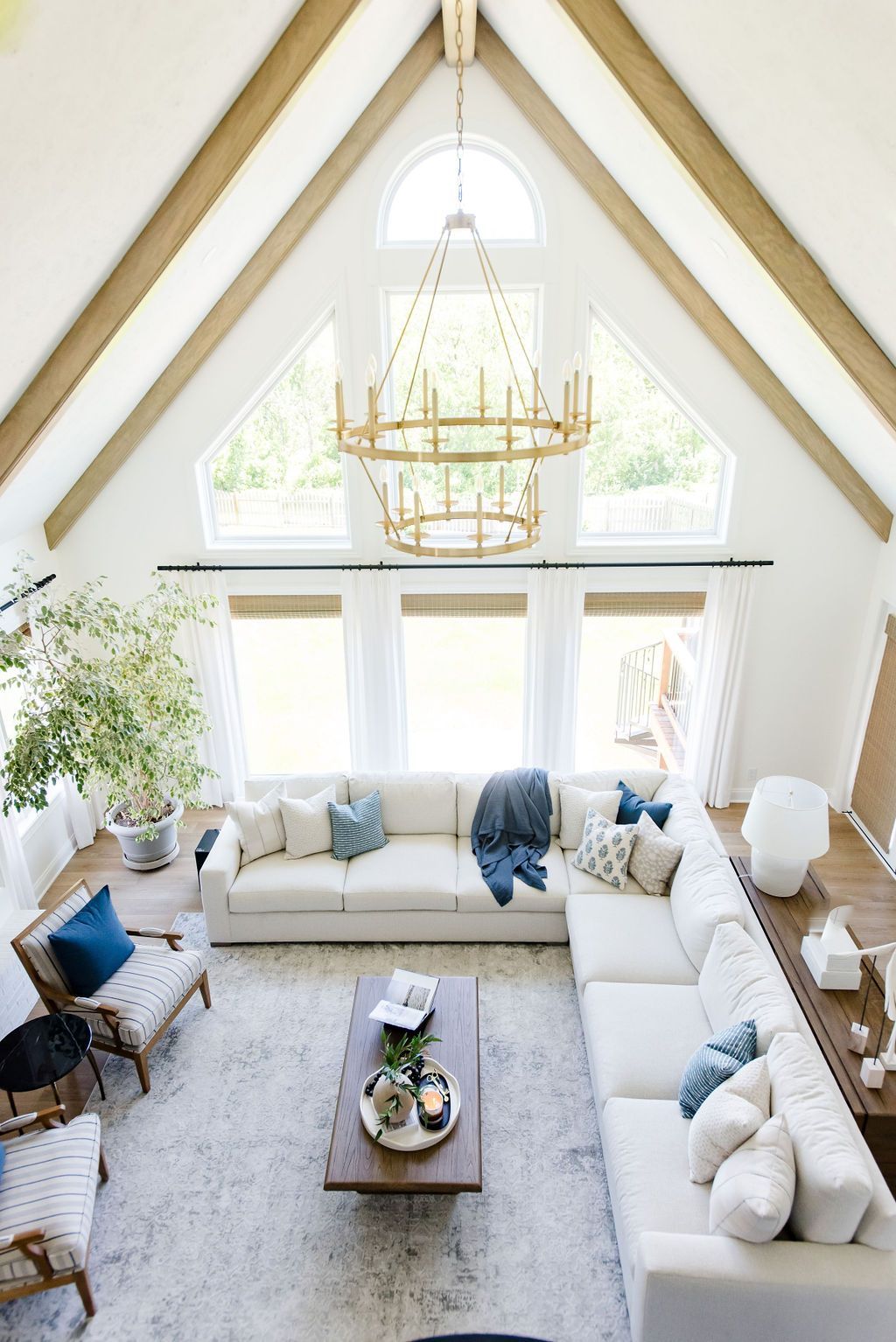 Bright vaulted living room with white sectional, gold chandelier, large windows, and blue accents