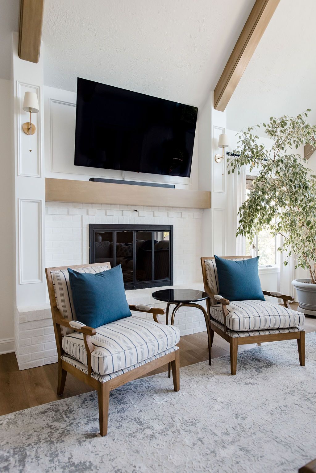 Bright living room with a fireplace, wall-mounted TV, and two cushioned chairs with blue pillows