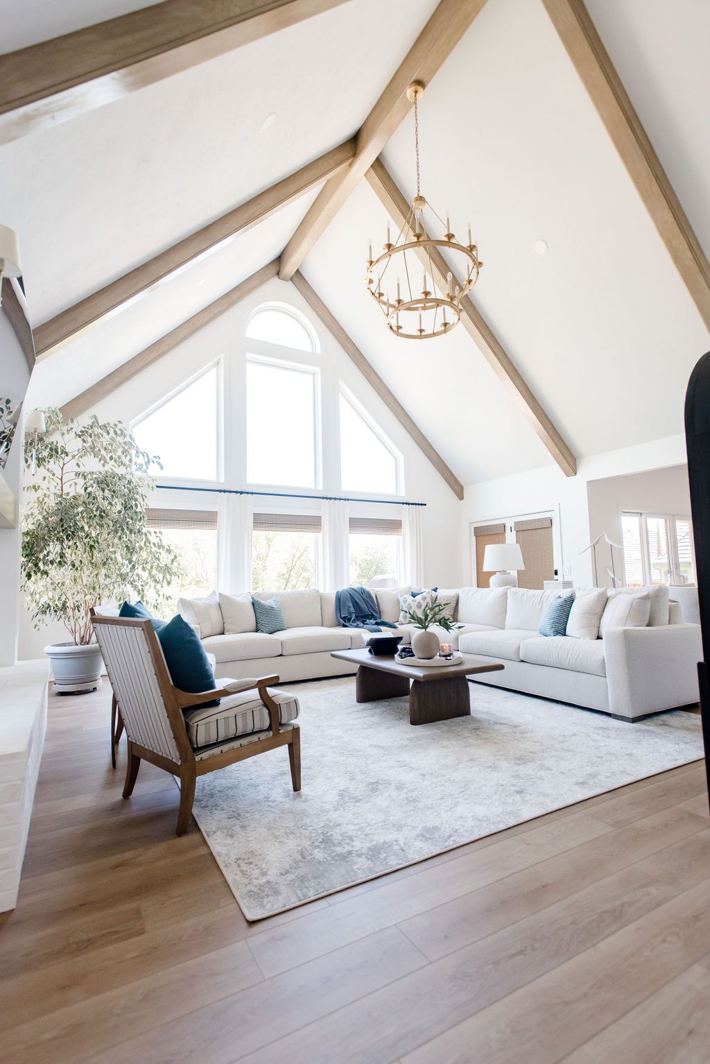 Bright, airy living room with vaulted white ceiling, chandelier, white sofa, wicker chair, and large windows.