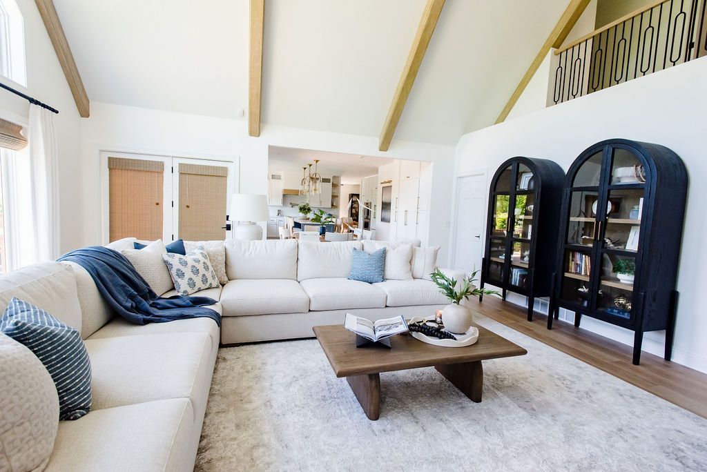 Bright living room with white sectional sofa, wooden coffee table, and black glass cabinets under vaulted ceilings